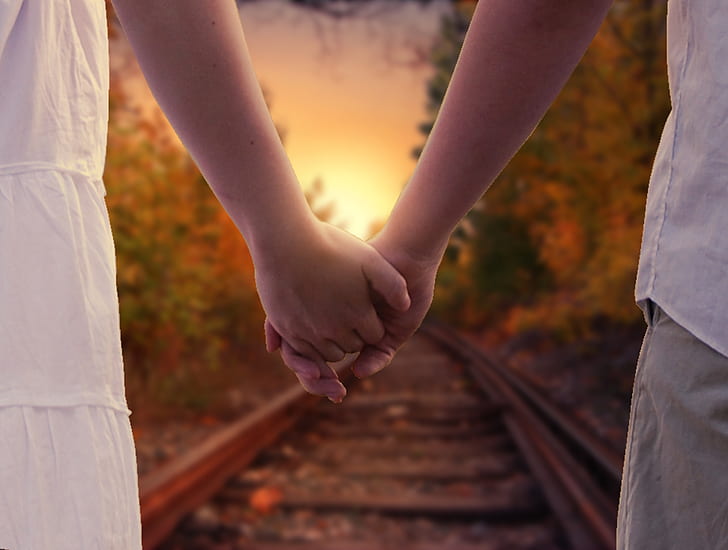 two people holding hands standing on train rail during daytime