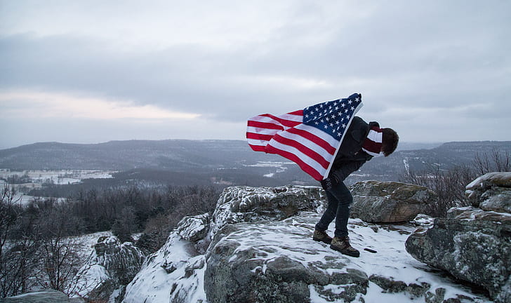 man holding USA flag on rock during daytime