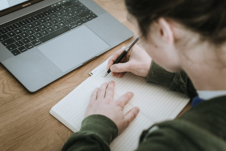woman writing on lined paper near MacBook Pro