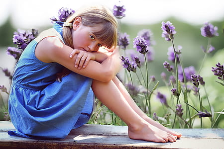 girl in blue sleeveless dress sitting on parquet bench near purple petaled flower field