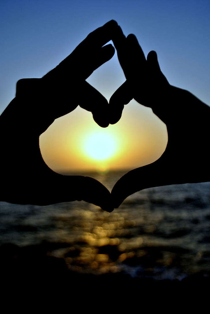 silhouette of two hands forming heart behind sunset