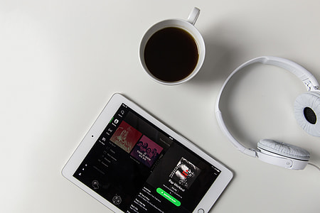 Headphones, coffee and iPad tablet with Spotify music app open on a white desk