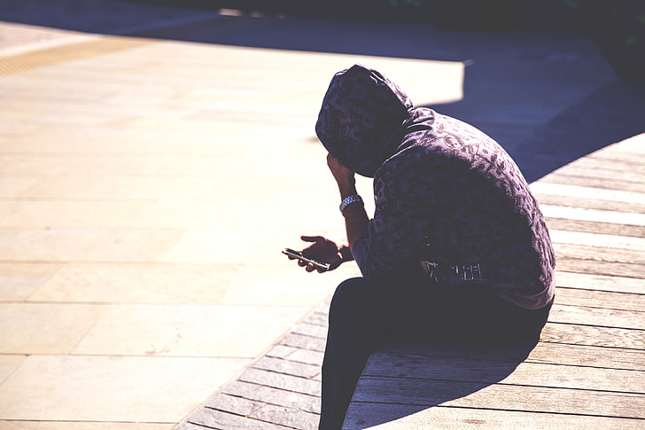 A man wearing a hoodie checks his mobile iPhone smartphone in an urban setting