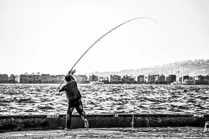 Grayscale Photography of Man Holding a Fishing Rod Near Body of Water