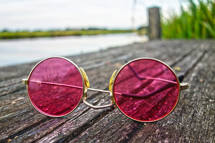 round silver-colored pink tinted sunglasses on grey wooden board