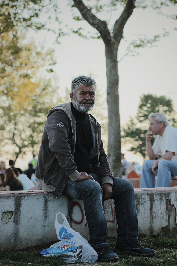 Man Wearing Gray Jacket Sitting on White Stone in Park during Day Time