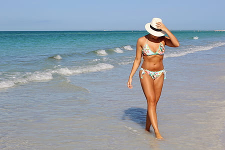 woman wearing white floral bikini walking beside sea at daytime