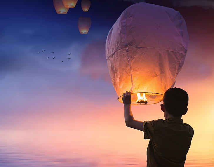 person holding floating lantern under sunset