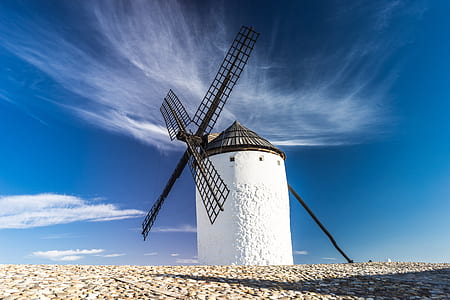 white lighthouse with black windmill under white clouds photography