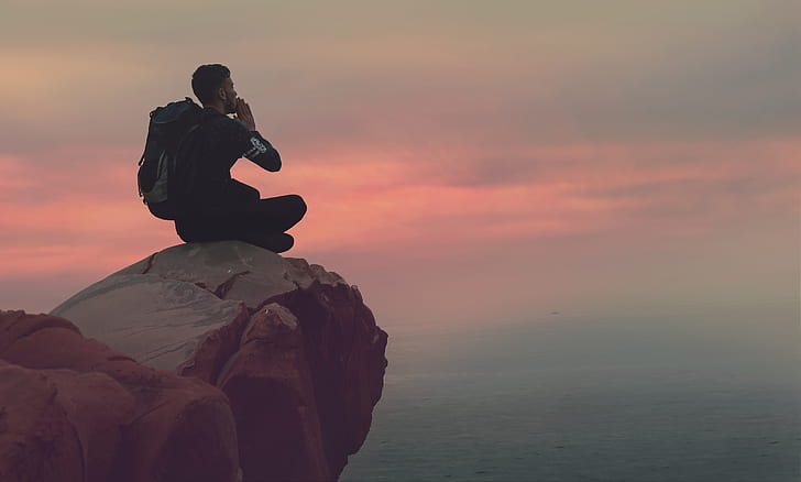 man sitting on mountain ledge at sunset