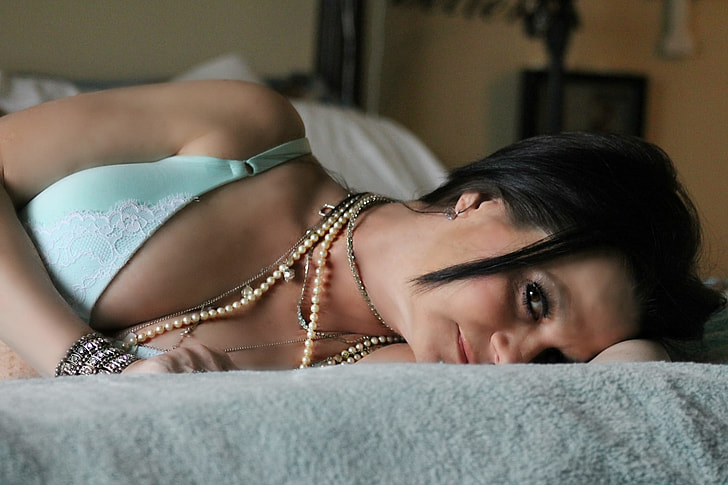 woman lying on bed wearing teal brassiere
