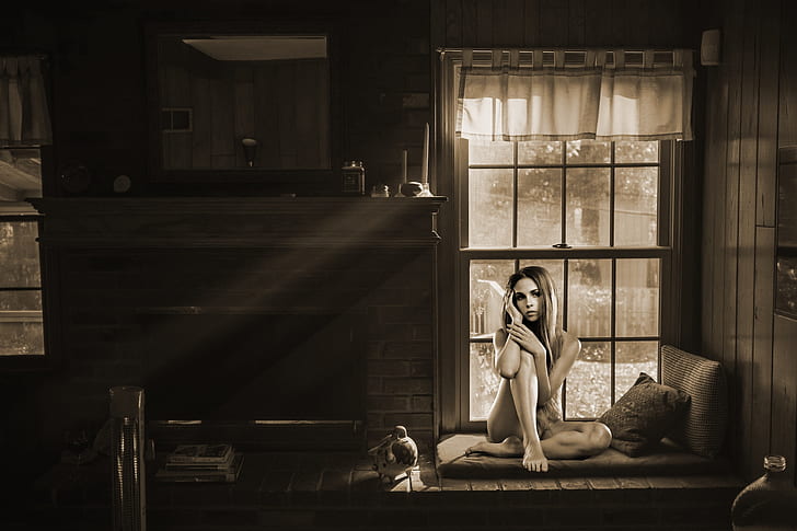 grayscale photo of woman sitting on sofa near window
