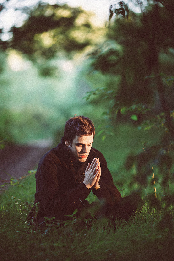 man wearing black jacket praying in forest