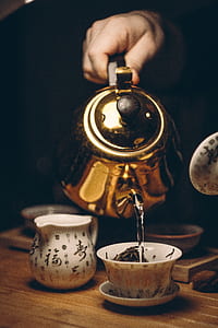 person holding brass kettle under white teacup on white saucer
