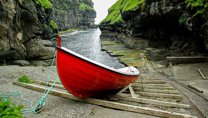 red and white rowboat near body of water surrounded by black mountain