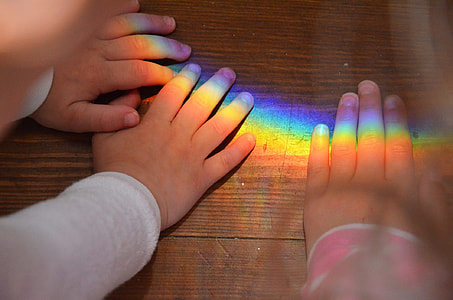 three person's hands placed on brown wooden surface with rainbow colored light