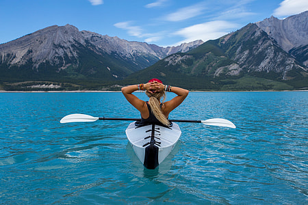 woman in white kayak on body of water within mountain range