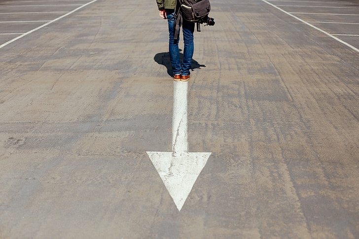person standing on gray and white concrete pavement with arrow