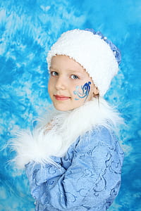 girl wearing blue floral faux-fur jacket and white knit cap with blue face paint