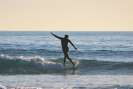 silhouette of person surfing on body of water during daytime