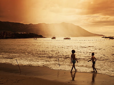 two children standing on shore during golden hour