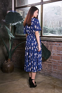 woman wearing blue and white floral dress facing window