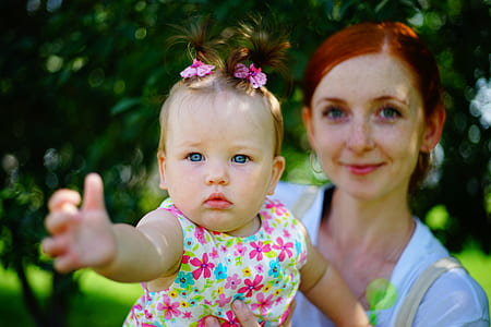 selective focus photo of woman carrying baby in floral sleeveless top