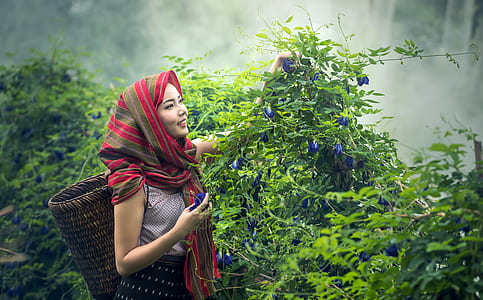 woman in white sleeveless top and red and brown striped headscarf holding green plants