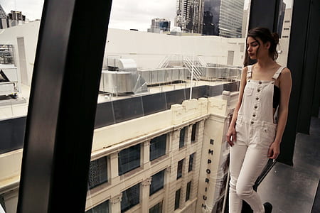 woman wearing white overalls leaning on window