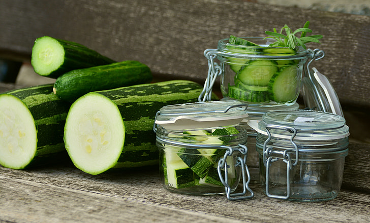 sliced green cucumber beside four clear glass jars on brown surface