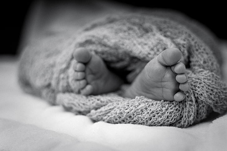 Greyscale Photo Of Human Feet Covered In Knitted Comforter