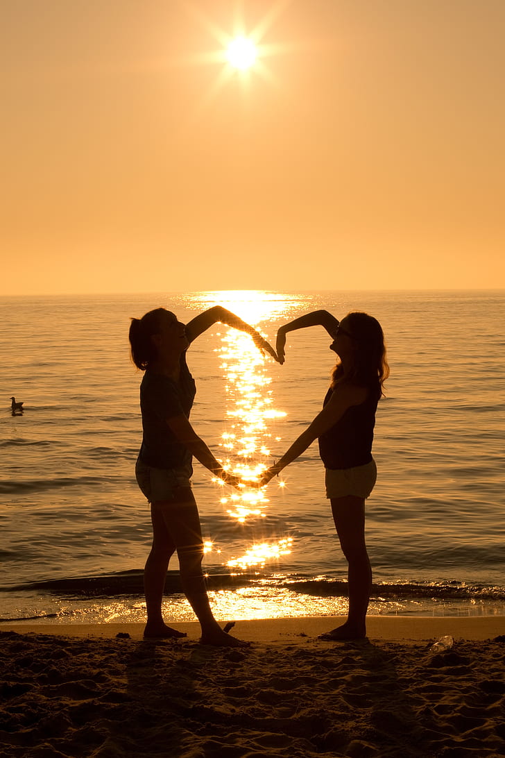 silhouette of two women forming heart during golden hour