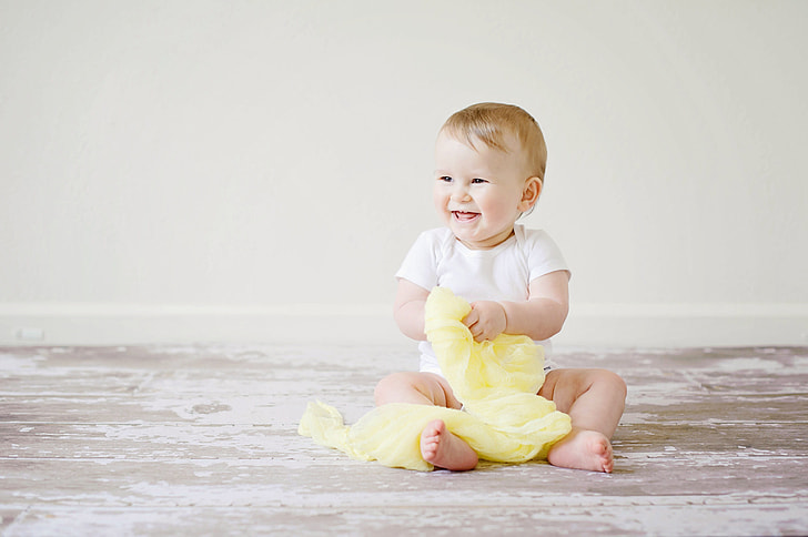 baby holding yellow textile while smiling