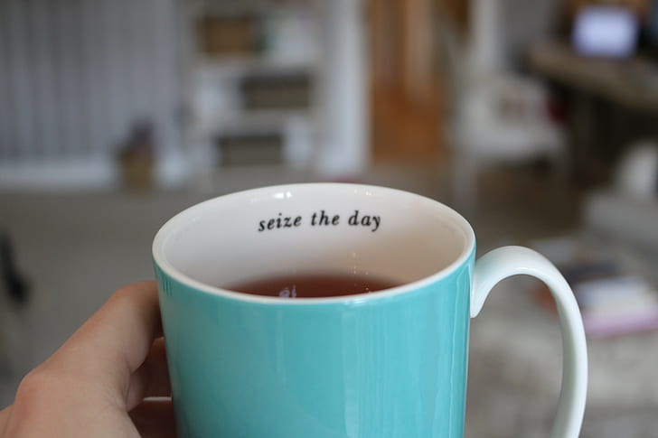 person holding white and teal ceramic mug