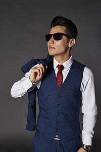 woman in blue button-up vest and white dress shirt with brown necktie wearing black sunglasses