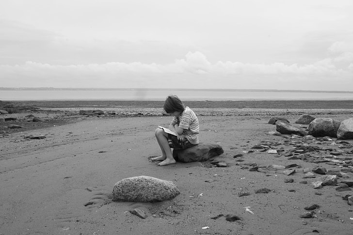 boy seating on rock at beach shore black and white photo
