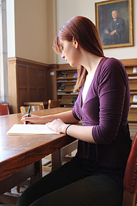 woman wearing purple v-neck shirt siting beside table while writing