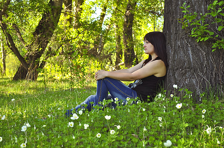 woman wearing black tank top and blue jeans leaning against tree