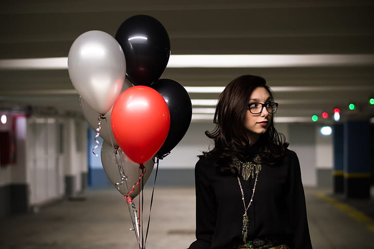 woman wearing eyeglasses and black top holding balloons on parking lot