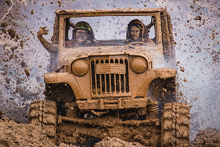 two men riding on mud covered wrangler during daytime