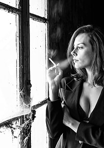 grayscale photo of smoking woman near window
