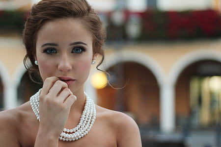 selective photo of woman with right hand on lips wearing pearl necklace
