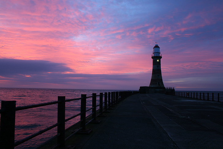 silhouette of lighthouse on wooden dock under pink and blue sky