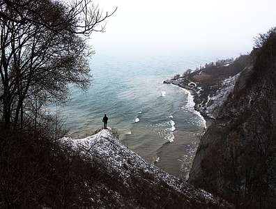 person standing on top of hillside looking on shoreline during daytime
