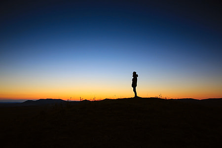 silhouette photo of a person standing on stone during sunset