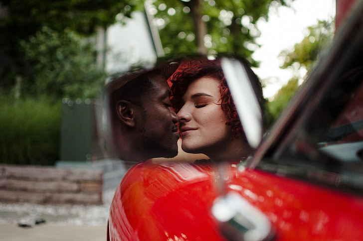 selective photo of couple kissing on the side mirror view