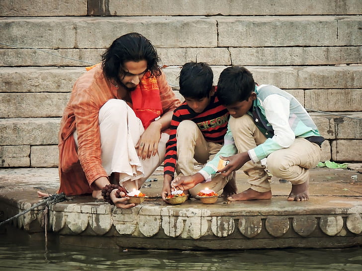 man and two boys sitting holding candles beside body of water