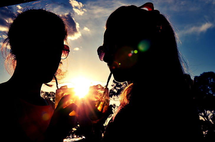 silhouette of two women zipping drinks during golden hours