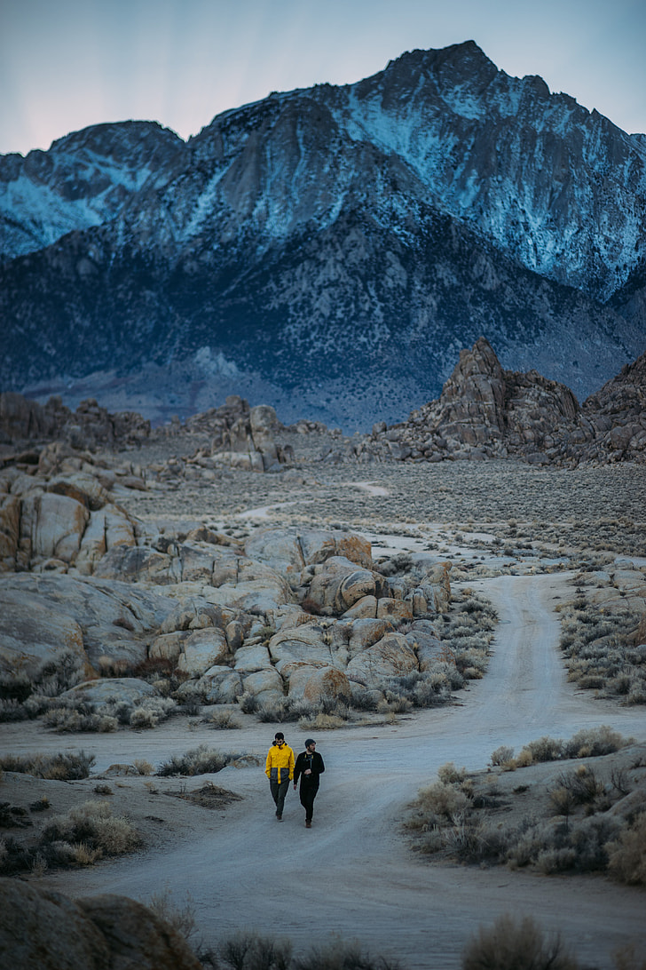 Two person walking on pathway surrounded by rocks