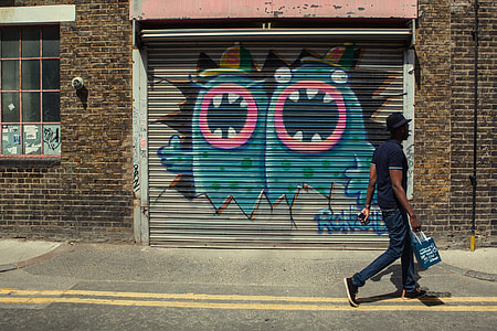 Street photo of a London man with a shopping bag. East London street art can be seen in the background